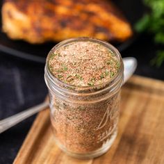 a jar filled with seasoning sitting on top of a wooden cutting board next to meat