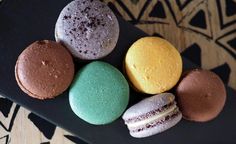 four different colored macaroons on a black plate