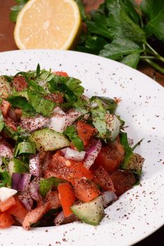 a white plate topped with lots of veggies and seasoning next to a lemon wedge