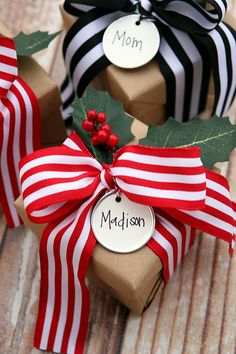 three wrapped present boxes with personalized tags and holly leaves on them, sitting on a wooden surface