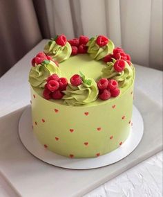 a yellow cake with raspberries and green icing on a white platter