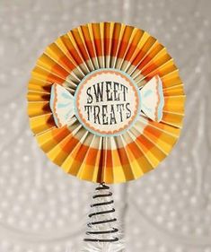 an orange and yellow pinwheel with the words sweet treats written on it, sitting in front of a white wall