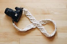 a camera is laying on the floor next to a white knitted strap that holds a black camera