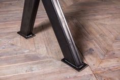 a wooden table with metal legs and a black base on the floor in front of it