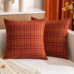 two orange plaid pillows sitting on top of a couch next to a vase with flowers