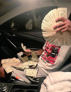 a man sitting in a car holding money and fanned out his hand to the camera