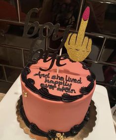 a pink birthday cake with black lettering and a hand holding a lit candle on top