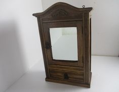 an old wooden cabinet with a mirror on it's front and bottom shelf, against a white wall