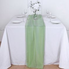 the table is set with white flowers in a vase on top of it, along with plates and glasses