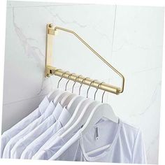 several white shirts hanging on a rack in front of a marble wall with a gold coat hanger