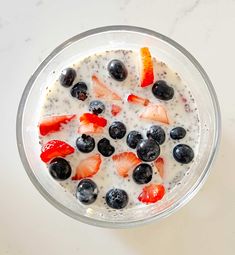 a bowl filled with fruit and milk on top of a white counter next to a spoon