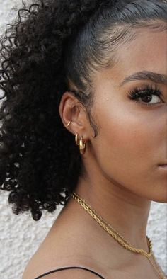 a close up of a woman with curly hair wearing gold earrings and a black tank top