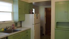 a kitchen with green cabinets and white counter tops, along with a small refrigerator freezer