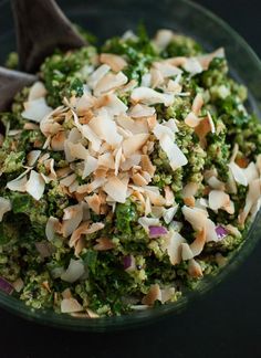 a glass bowl filled with broccoli and almonds next to a wooden spoon