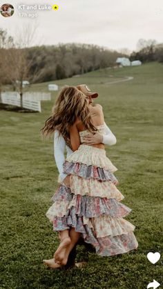 two women hugging in the middle of a field with one woman wearing a dress and hat