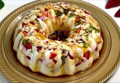 a bundt cake covered in fruit and nuts on a gold plate next to strawberries