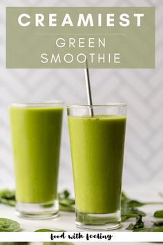 two glasses filled with green smoothie on top of a white table next to leaves