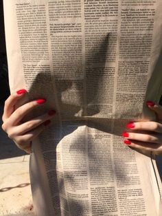 a woman with red nail polish holding an open book in front of her face and hands