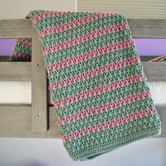 a crocheted green and pink blanket hanging from a wooden rail next to a bed