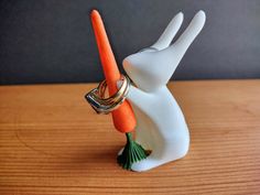 a white bunny holding an orange carrot on top of it's back with its mouth open