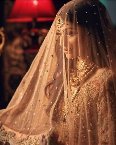 a woman wearing a veil and gold jewelry is standing in front of a red lamp