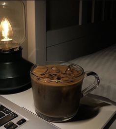 a cup of coffee sitting on top of a desk next to a laptop computer and lamp