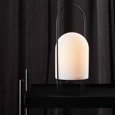 a white lamp sitting on top of a black table next to a curtained window