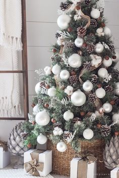 a christmas tree with white ornaments and pine cones in baskets next to presents on the floor