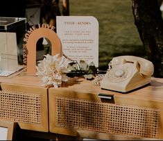 an old fashioned phone sitting on top of a wooden table next to a sign and flowers