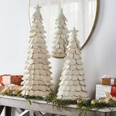 two white christmas trees sitting on top of a wooden table next to presents and a mirror