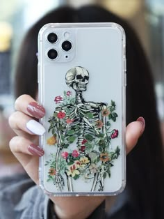 a woman holding up a clear phone case with a skeleton and flowers on the back