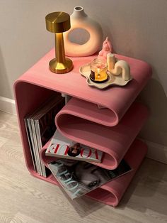 a pink shelf with magazines and vases on it next to a wall mounted lamp