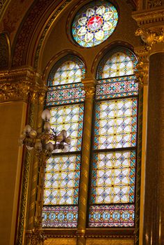 two stained glass windows in the middle of a room with columns and chandeliers