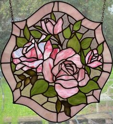 a stained glass window with pink roses on it and green leaves in the center, hanging from chain