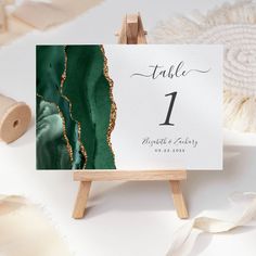 an easel with a table number on it next to some white and green decorations