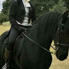 a woman riding on the back of a black horse in a field next to trees