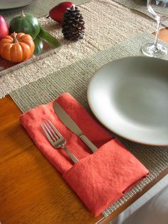 a place setting with silverware and napkins on a wooden table next to pine cones