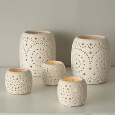 four white vases with holes on them sitting next to each other in front of a wall