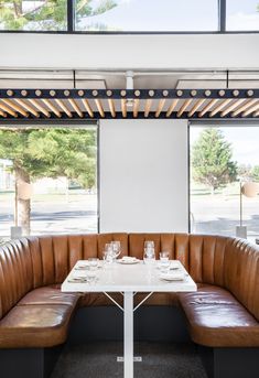 a table with two glasses on it in front of a window and some brown leather booths