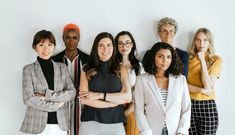 a group of women standing next to each other in front of a white wall with their arms crossed