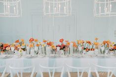 a long table is set with white chairs and colorful flowers in vases on it