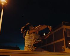 a woman is sitting on the roof of a car at night with her arms outstretched