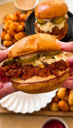 a person holding a sandwich in front of some other food on a plate with sauce and ketchup