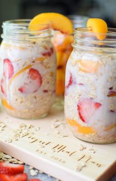 two mason jars filled with oatmeal and strawberries on top of a cutting board