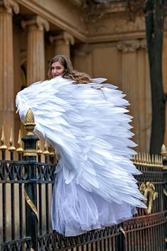 a woman dressed as an angel standing next to a fence with her wings spread out