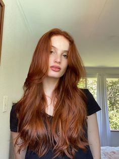 a woman with long red hair standing in front of a window and looking at the camera