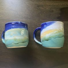 two coffee mugs sitting on top of a wooden table with blue and green designs