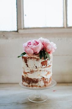 a cake with frosting and flowers on top sitting on a table next to a window