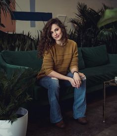 a woman sitting on top of a green couch next to potted plants and a table