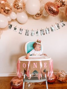 a baby in a highchair surrounded by balloons and streamers for a first birthday party